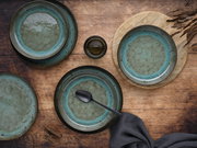 Vogelperspektive auf ein 12-teiliges Tafelservice mit grün-blauen Tellern und Schalen auf einem Holztisch, dekoriert mit einem schwarzen Löffel und einem grauen Tuch.