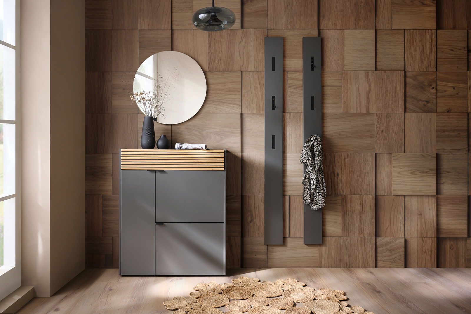 Voleo Schuhschrank RIO Moderner Schuhschrank Voleo Mehrzweckschrank RIO in grauer Farbe mit Holzdetails, frontal abgebildet in einem stilvollen Raum mit Holzwand und runden Dekorationselementen.