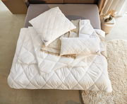 Luftaufnahme eines gemütlichen Bettes mit weißem, gestepptem Ganzjahresbett 155x220 cm, zwei passenden Kissen und einer beigen Decke.