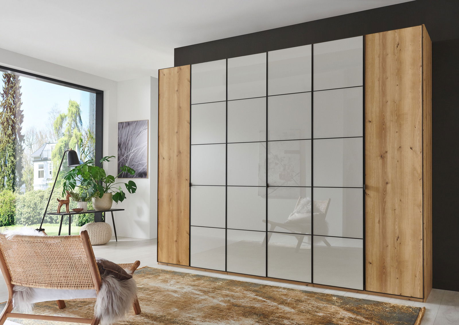 Moderner Drehtürenschrank mit Holz- und Glaselementen, frontal abgebildet in einem hellen Raum mit großen Fenstern.