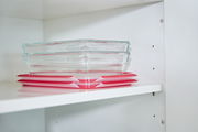Zwei rechteckige Glasbehälter mit roten Deckeln, gestapelt in einem weißen Regal, seitliche Perspektive.