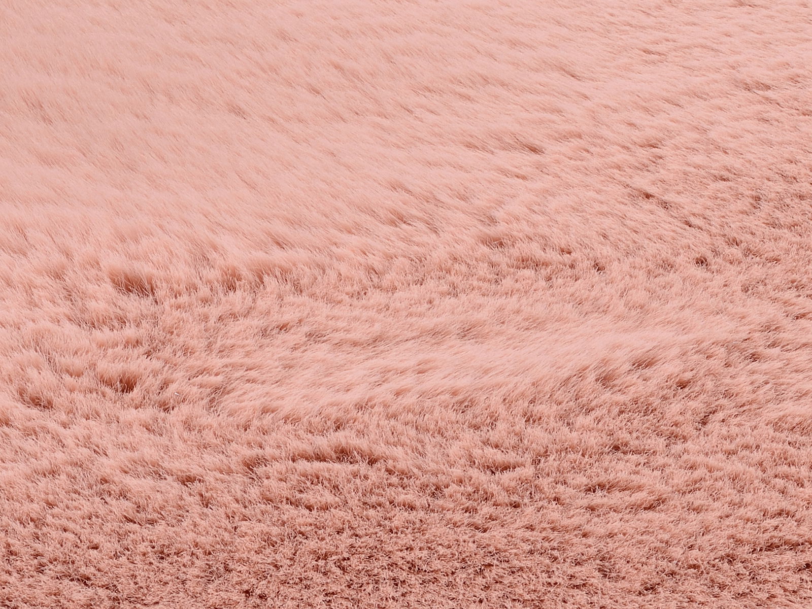 Nahaufnahme eines rosafarbenen Fellteppichs mit weicher, flauschiger Textur, von schräg oben betrachtet.