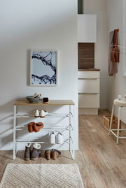 Weißes Schuhregal mit Holzablage und mehreren Ablagen, im Flur mit Schuhen dekoriert, frontal aus leicht erhöhter Perspektive fotografiert.