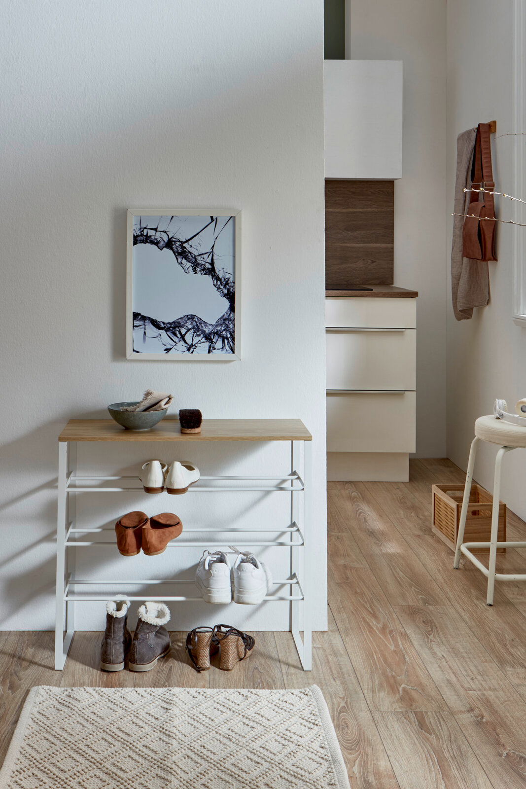 Weißes Schuhregal mit Holzablage und mehreren Ablagen, im Flur mit Schuhen dekoriert, frontal aus leicht erhöhter Perspektive fotografiert.