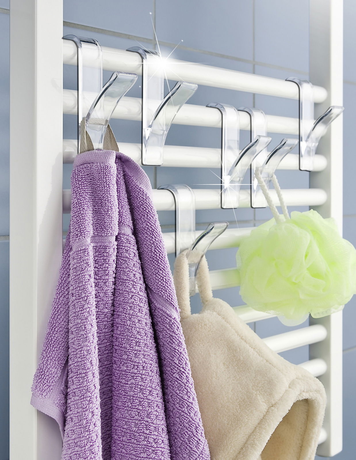 Transparente Haken für Handtuchheizkörper, frontal fotografiert, mit aufgehängten Handtüchern und Duschschwamm.