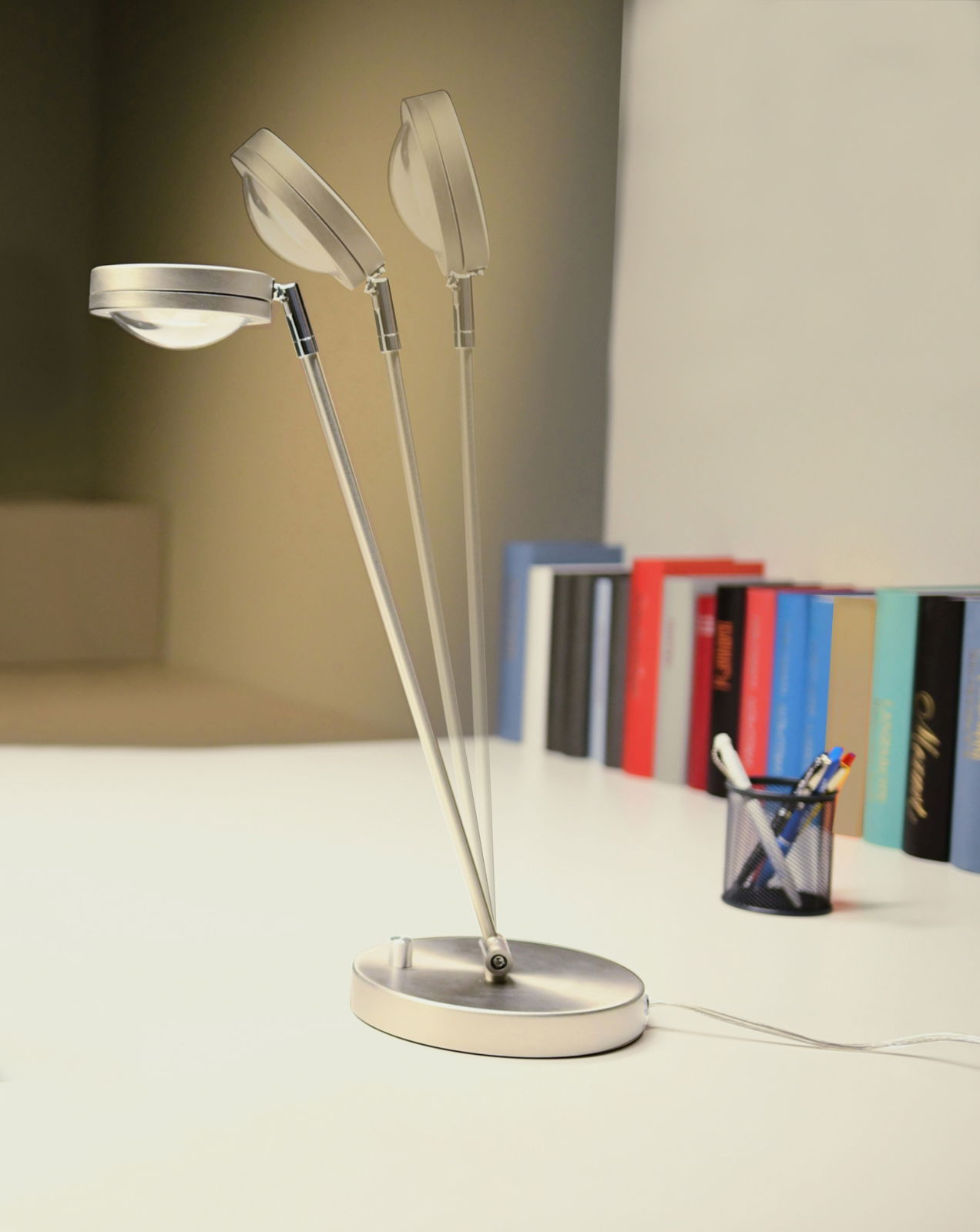 Moderne LED Tischleuchte mit verstellbarem Kopf, seitliche Perspektive, auf einem Schreibtisch mit Büchern und Stiftehalter.