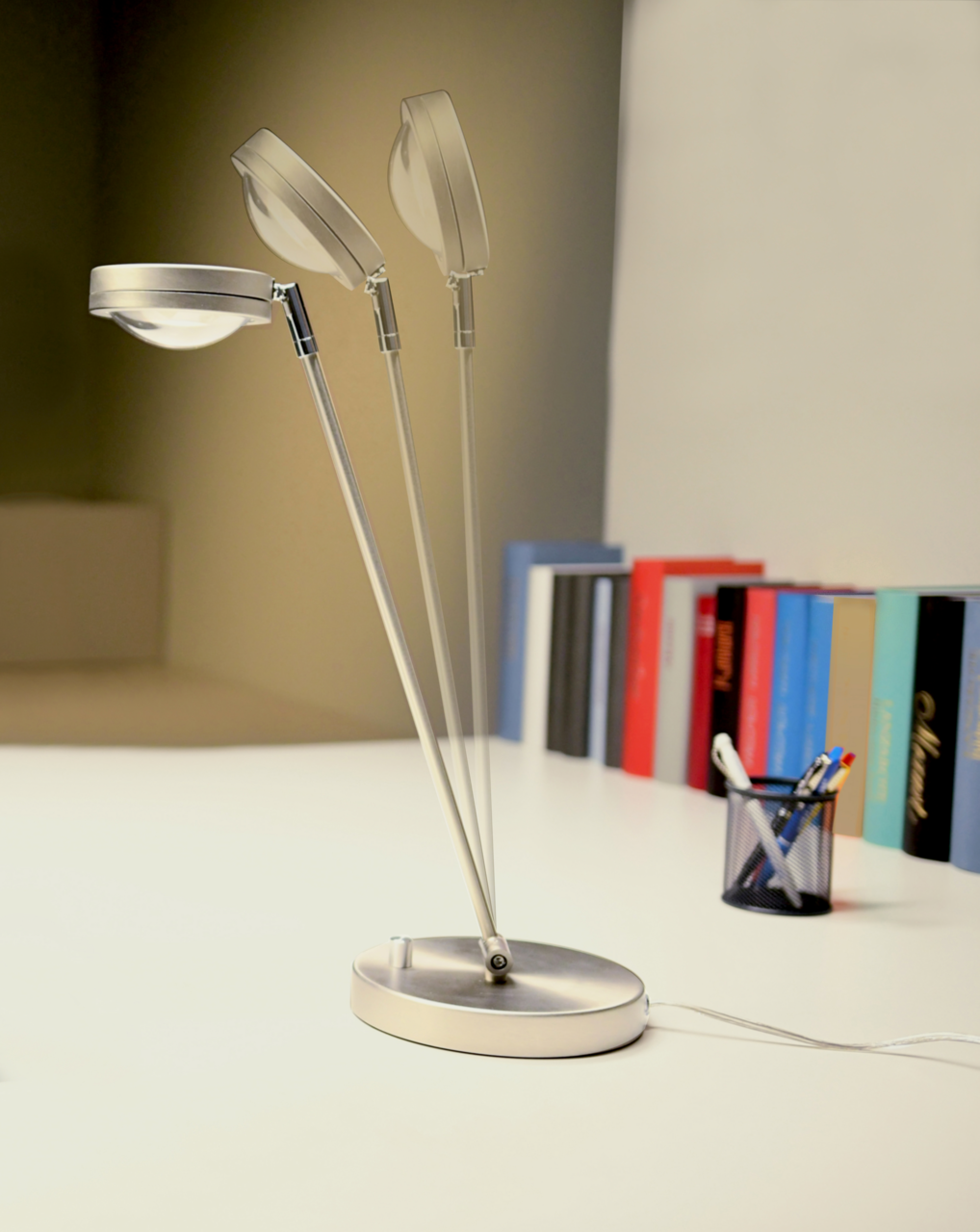 Moderne LED Tischleuchte mit verstellbarem Kopf, seitliche Perspektive, auf einem Schreibtisch mit Büchern und Stiftehalter.