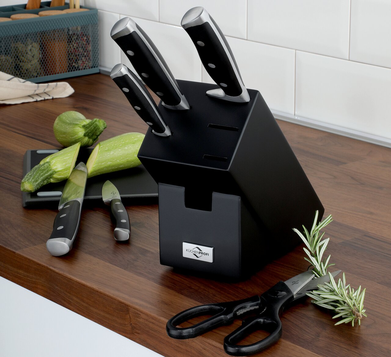 Schwarzer Messerblock PRIMUS CLASSIC mit sieben Steckplätzen, drei Messer und eine Schere sichtbar, auf einer Küchenarbeitsplatte aus Holz, seitliche Perspektive.
