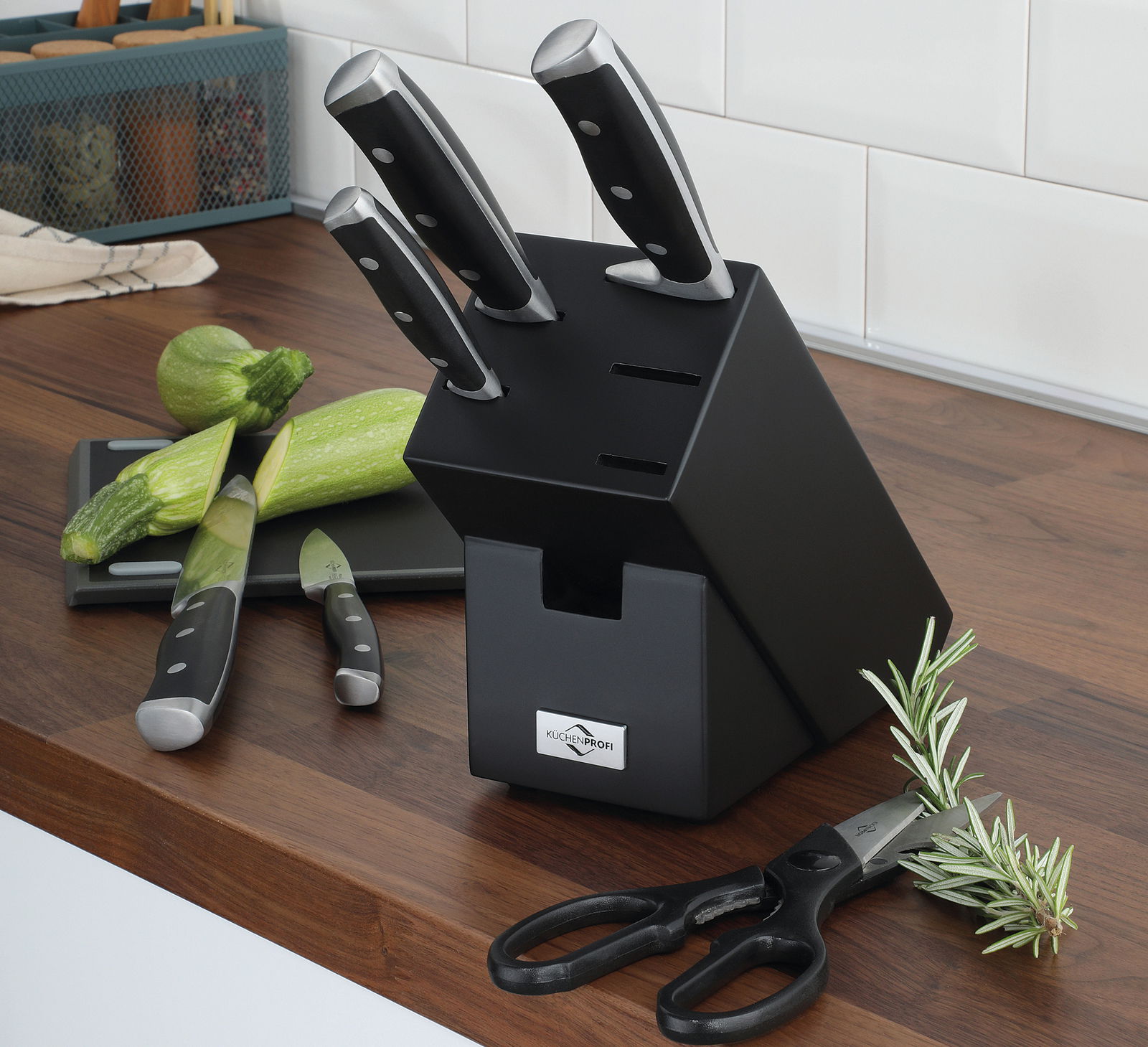 Schwarzer Messerblock PRIMUS CLASSIC mit sieben Steckplätzen, drei Messer und eine Schere sichtbar, auf einer Küchenarbeitsplatte aus Holz, seitliche Perspektive.