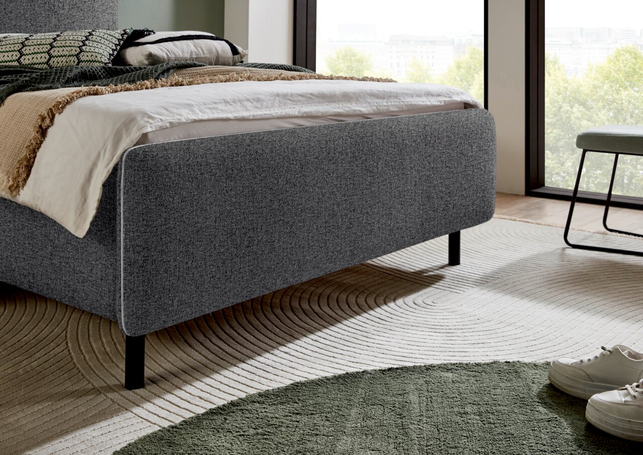 Graues Polsterbett in einem modernen Schlafzimmer, seitliche Perspektive