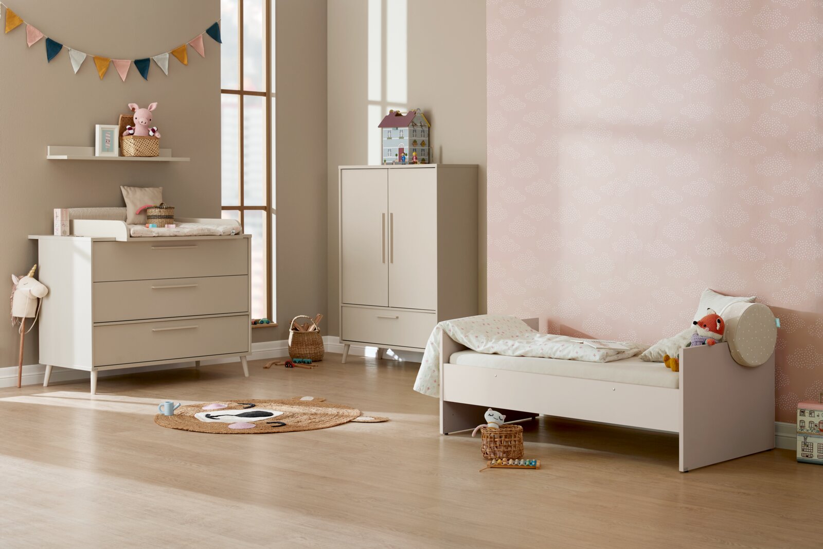 Paidi Wandplank EEFJE Kinderkamerinterieur met beige babybedje, commode en kledingkast, pastelroze wolkenbehang en houten vloer, gefotografeerd in schuin zijaanzicht (breedbeeld) vanaf ooghoogte.