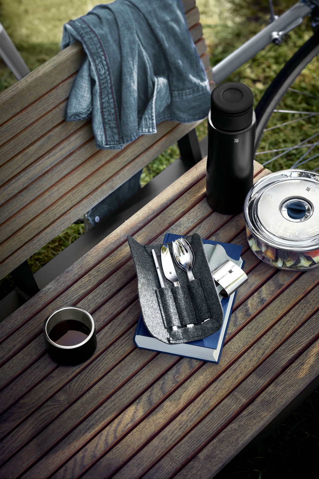 Besteck-Set My2Go auf einer Parkbank, bestehend aus Messer, Gabel und Löffel in einer Filztasche, neben einer Thermoskanne und einem Salatbehälter.