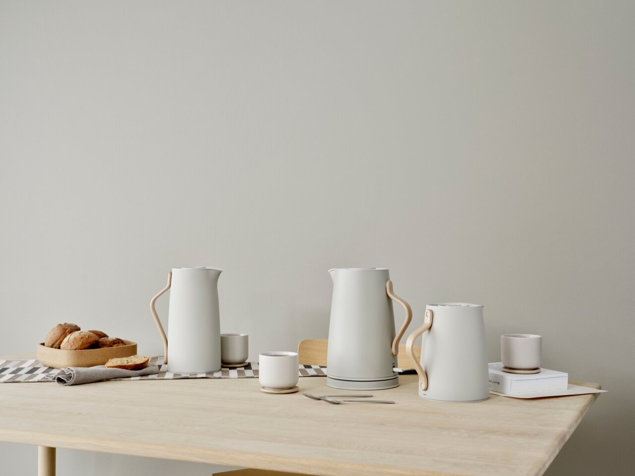 Stelton Wasserkocher EMMA Moderner Wasserkocher in elegantem Design mit Holzgriff, auf einem Tisch mit Tassen und Gebäck, seitliche Perspektive.