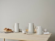 Moderne waterkoker in een elegant ontwerp met houten handvat, op een tafel met kopjes en gebak, zijaanzicht.