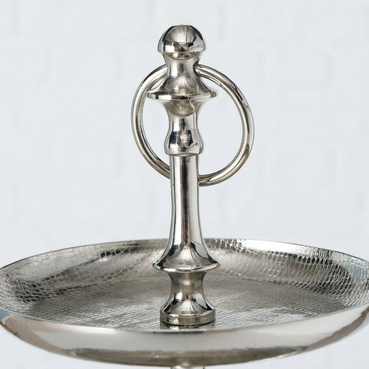 Nahaufnahme einer silbernen Etagere aus der Serie PASSIA von AluBoltze, mit einem eleganten, glänzenden Finish und einem dekorativen Griff. Perspektive von oben auf die obere Ebene.