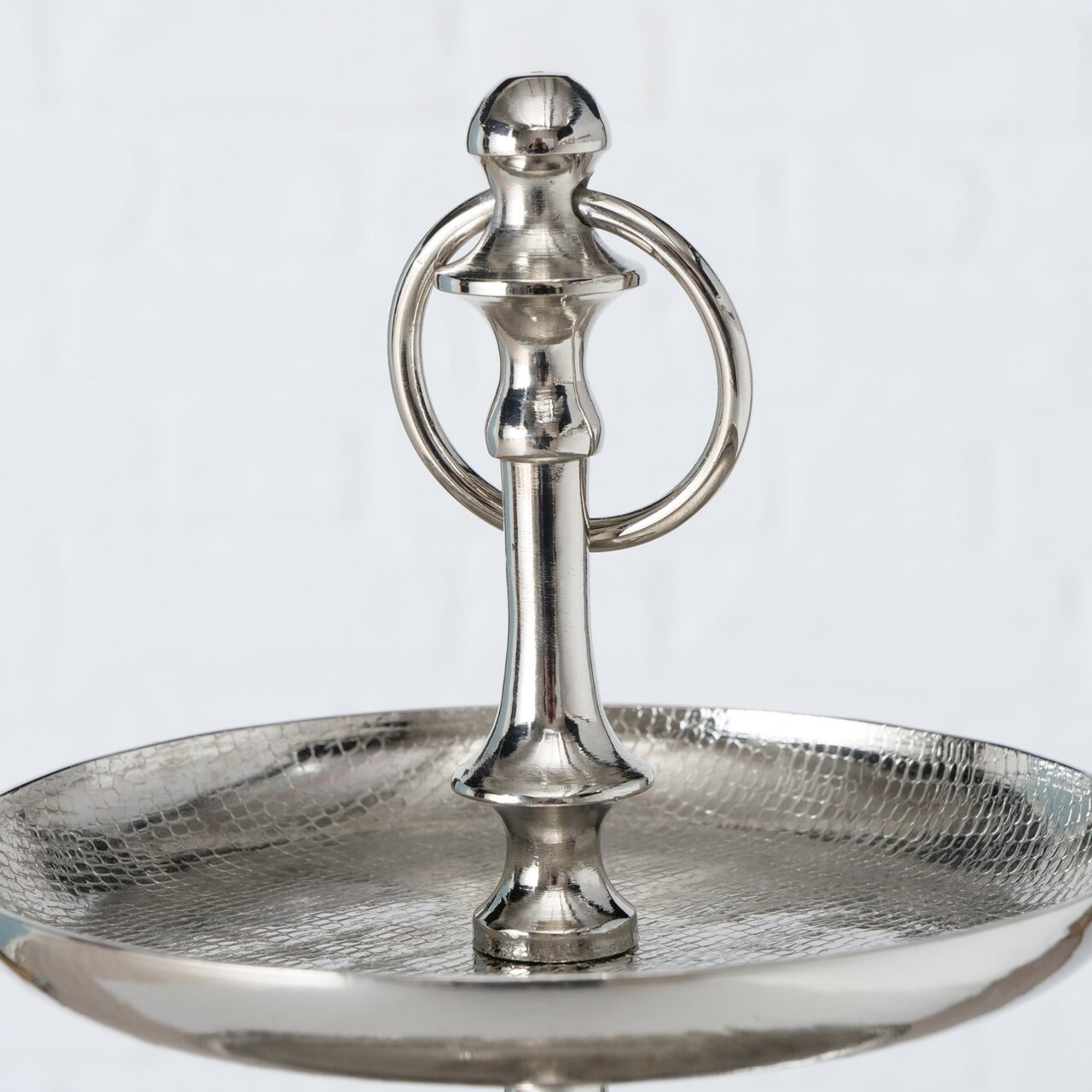 Nahaufnahme einer silbernen Etagere aus der Serie PASSIA von AluBoltze, mit einem eleganten, glänzenden Finish und einem dekorativen Griff. Perspektive von oben auf die obere Ebene.