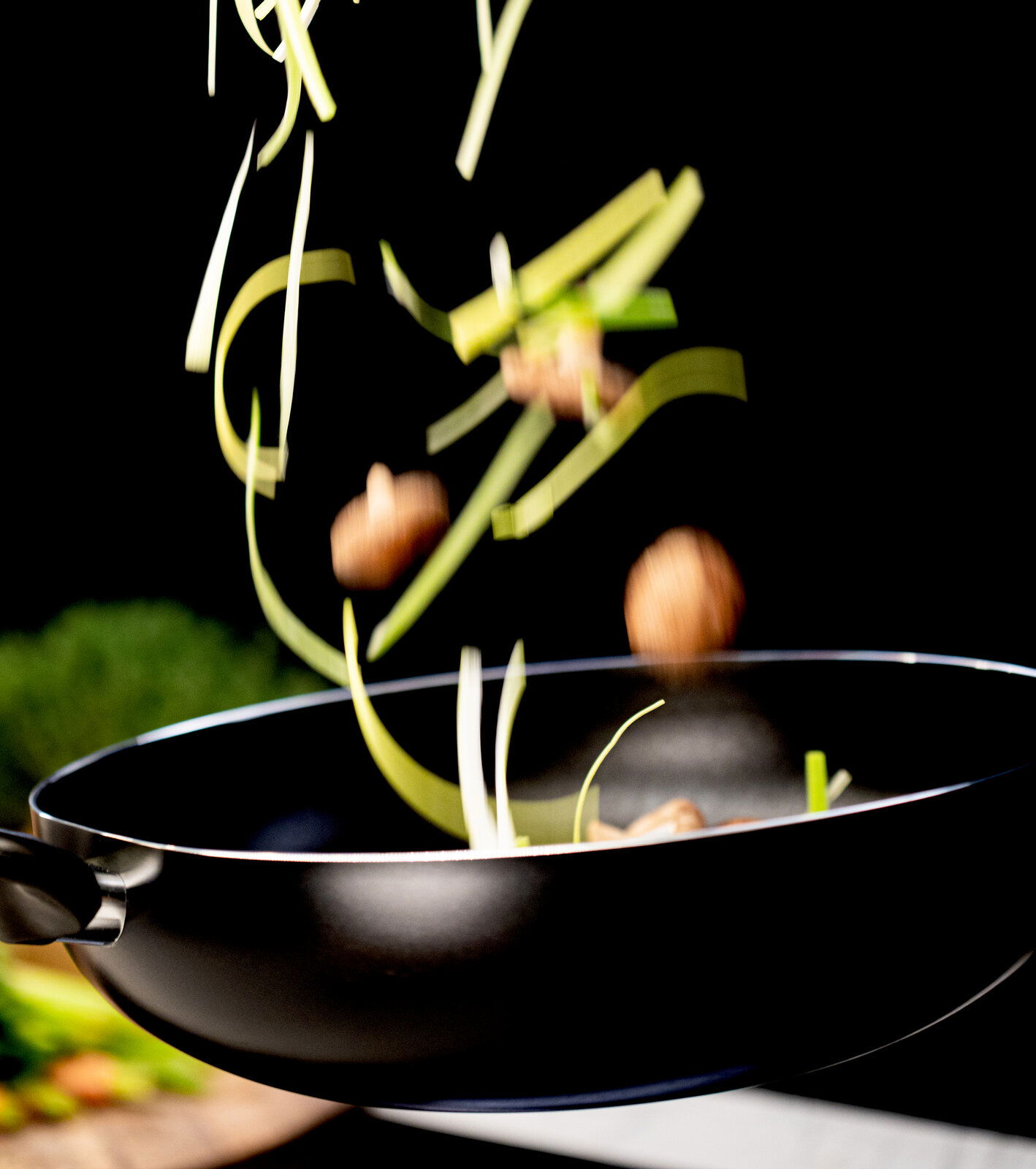 Wok-Pfanne in seitlicher Perspektive mit fliegendem Gemüse und Pilzen