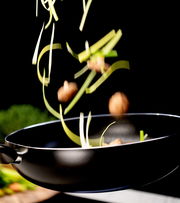 Wok-Pfanne in seitlicher Perspektive mit fliegendem Gemüse und Pilzen