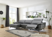 Graue Longchairkombination mit drei Sitzen, rechter Longchair und verstellbarem Fußteil, in einem modernen Wohnzimmer mit großen Fenstern und Pflanzen, seitliche Perspektive.
