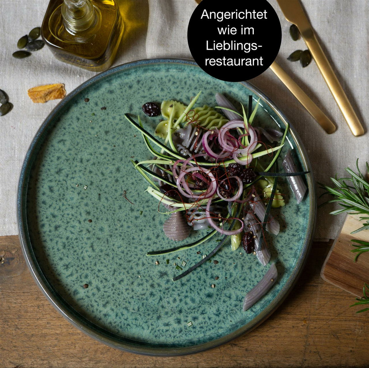 Grüner Teller mit elegant angerichtetem Salat aus Zwiebeln, Zucchini und getrockneten Früchten, von oben fotografiert.
