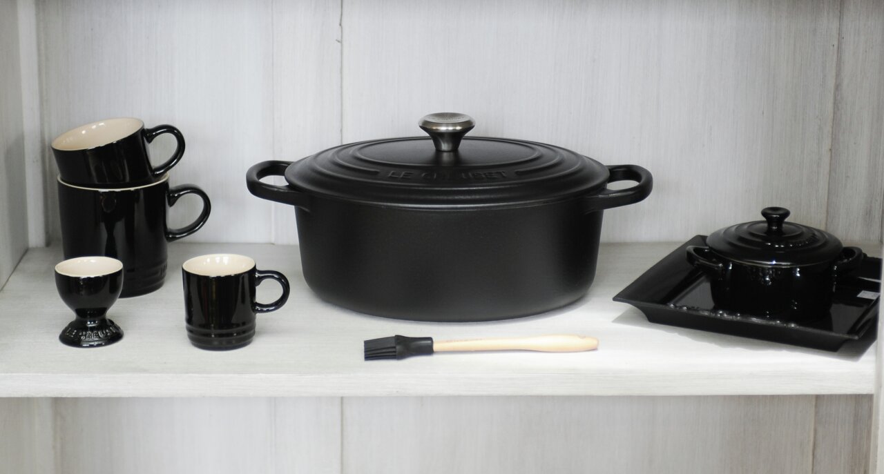 LE CREUSET Bräter Oval 29cm Schwarz SIGNATURE Schwarzer Bräter Ov Sig 29 cm in Frontalansicht, umgeben von schwarzem Geschirr und Küchenutensilien.
