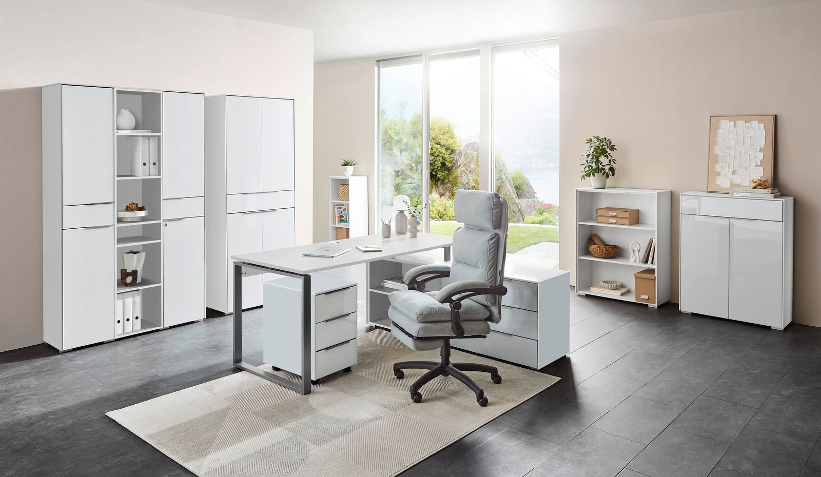 Voleo Aktenschrank Kombination NEVADA Moderne Büromöbelkombination mit Schreibtisch, Rollcontainer und Aktenschränken in einem hellen Raum mit Blick auf den Garten, aus der Perspektive von vorne.