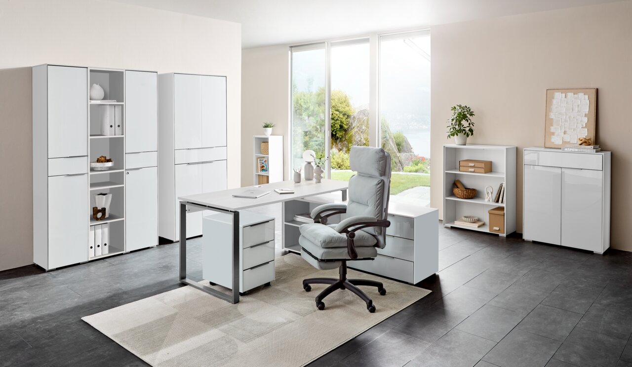 Moderne Büromöbelkombination mit Schreibtisch, Rollcontainer und Aktenschränken in einem hellen Raum mit Blick auf den Garten, aus der Perspektive von vorne.