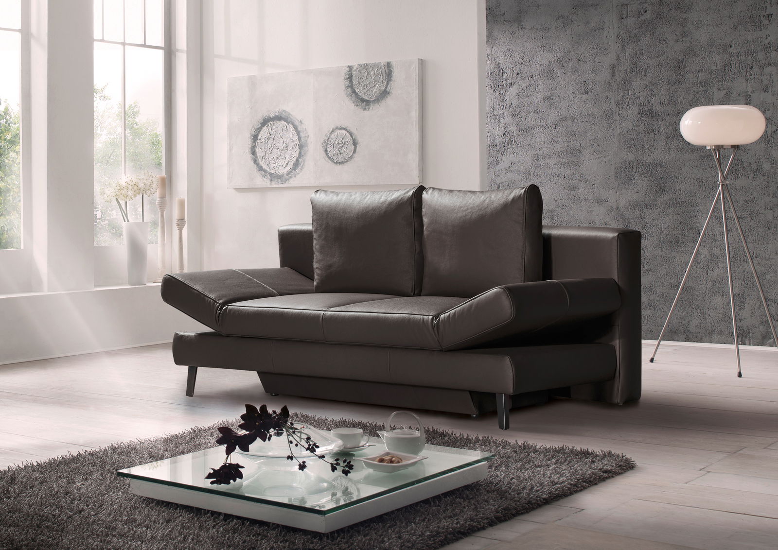Modernes Querschläfer-Sofa in dunklem Leder, seitliche Perspektive, in einem stilvoll eingerichteten Wohnzimmer mit großen Fenstern und dekorativen Elementen.
