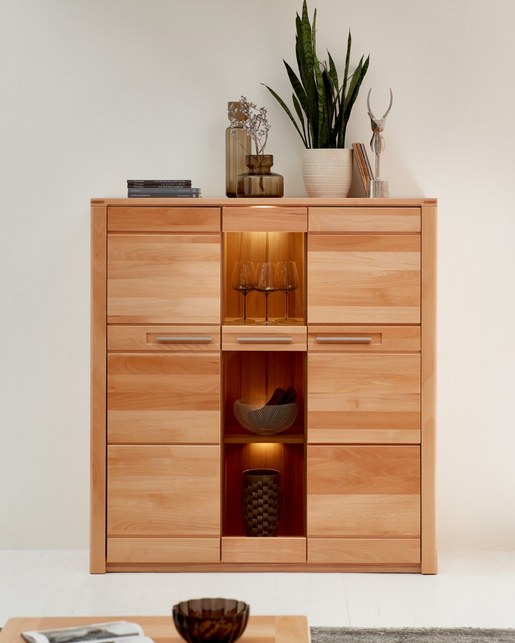 Vooraanzicht van een modern houten hoogkastje met meerdere lades en open vakken, versierd met planten en vazen.