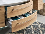 Badezimmerschrank mit zwei offenen Schubladen aus Holzoptik, gefüllt mit Handtüchern und Accessoires, aus seitlicher Perspektive.