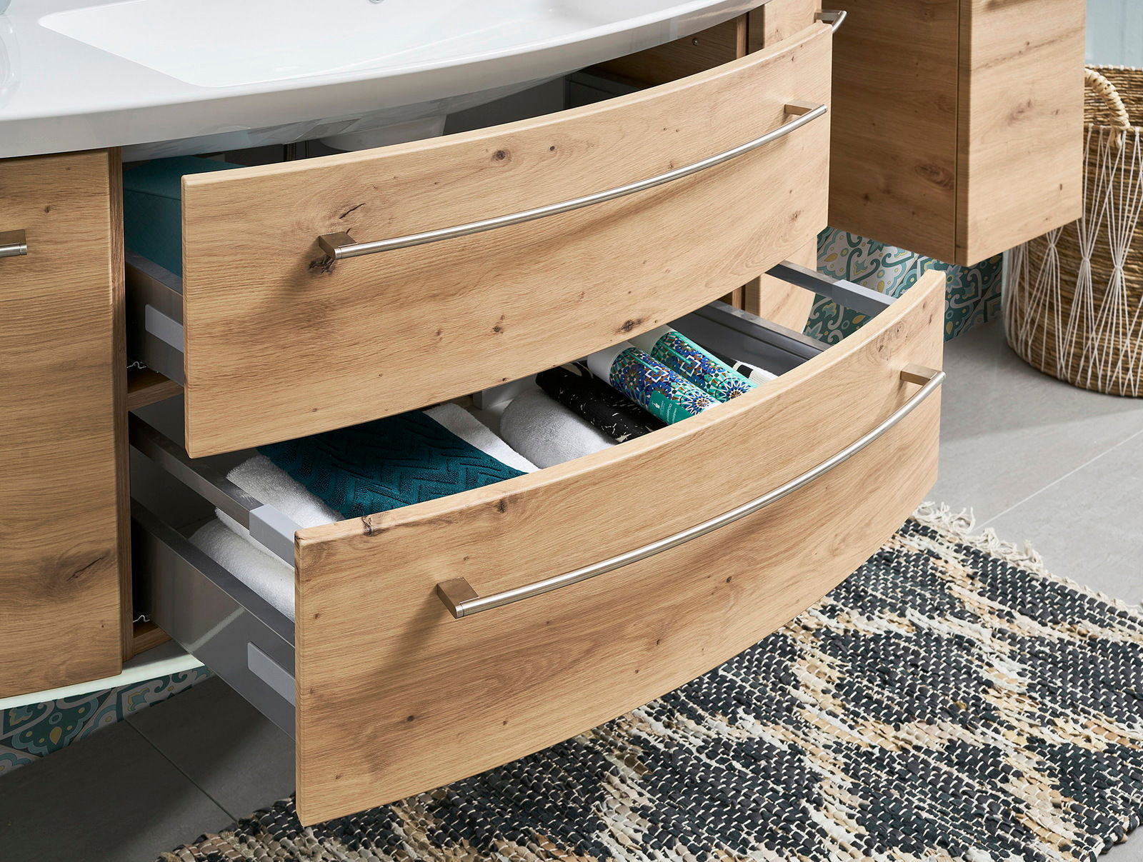 Badezimmerschrank mit zwei offenen Schubladen aus Holzoptik, gefüllt mit Handtüchern und Accessoires, aus seitlicher Perspektive.