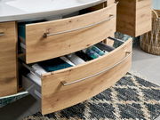 Badezimmerschrank mit zwei offenen Schubladen aus Holzoptik, gefüllt mit Handtüchern und Accessoires, aus seitlicher Perspektive.