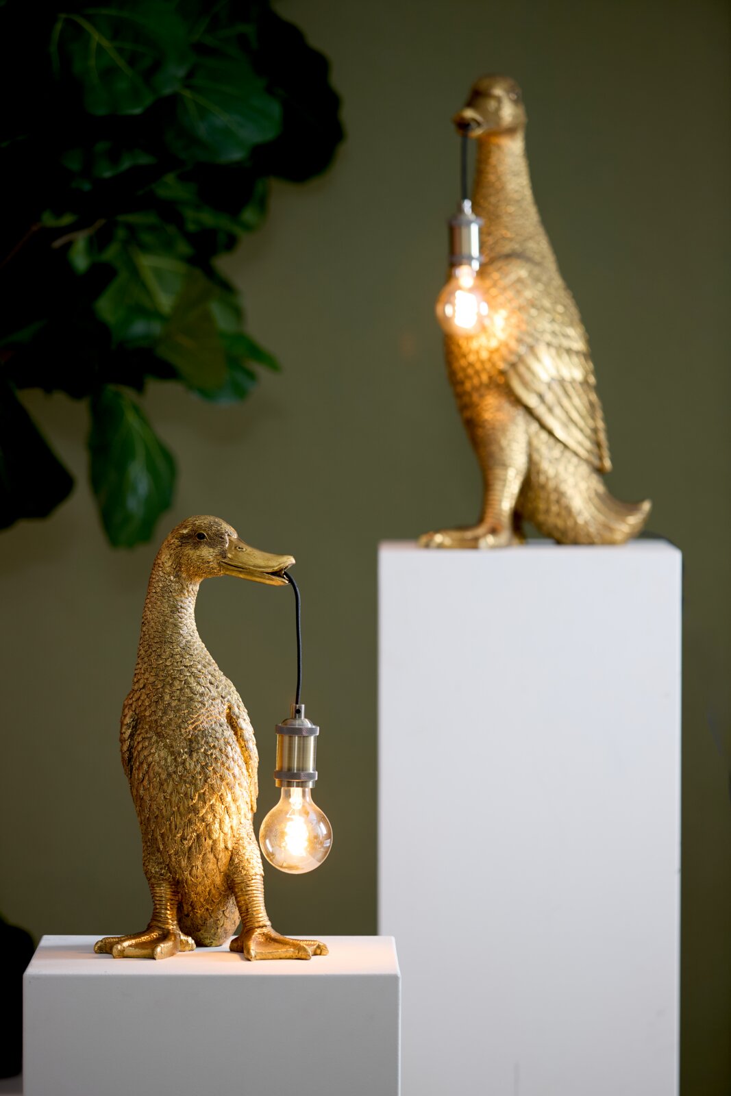 Goldene Tischleuchte in Form einer Ente, die eine Glühbirne im Schnabel hält, seitliche Perspektive.