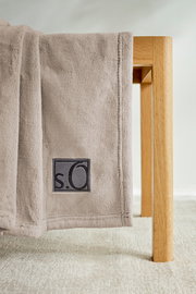 Beige Kuscheldecke von s.Oliver, drapiert über eine Holzstuhl, Nahaufnahme