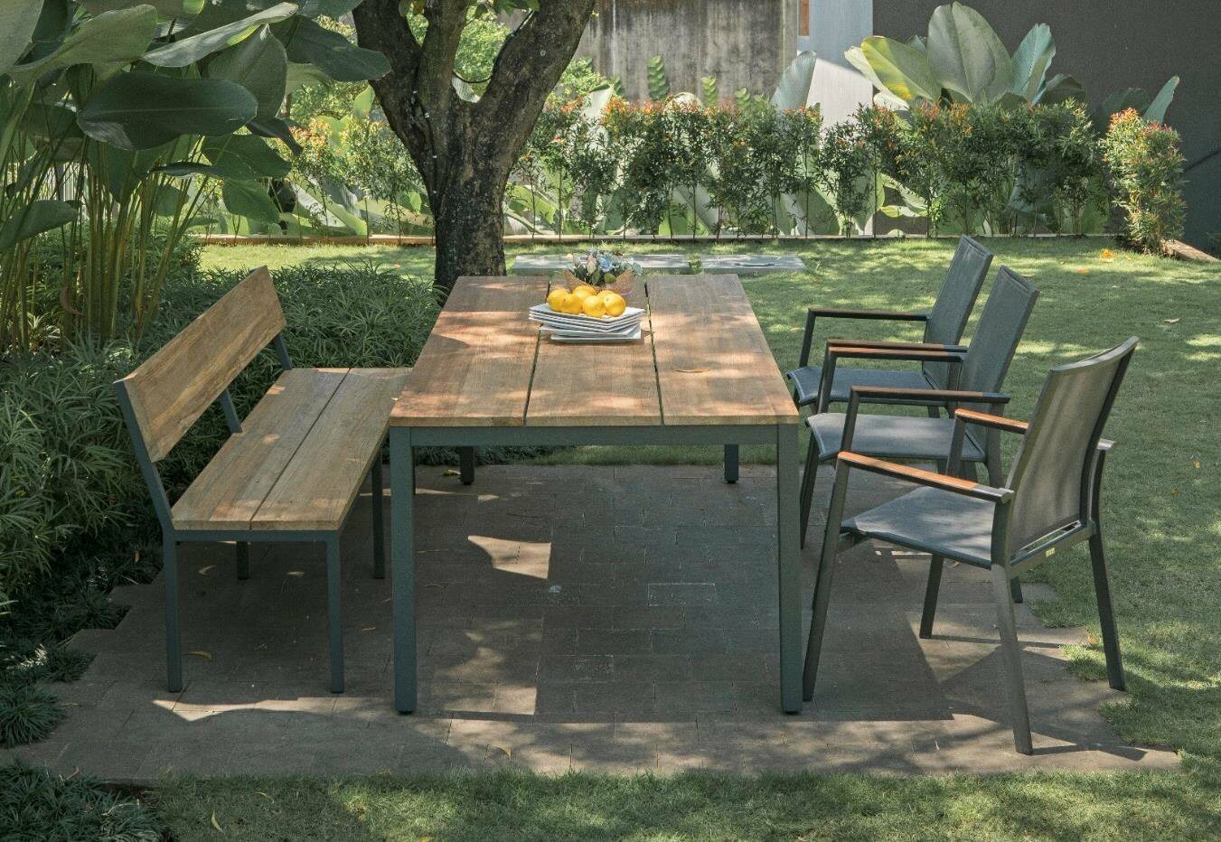 Gartenmöbel-Set mit einem Holztisch, einer Holzbank und drei Stapelsesseln aus Metall, seitliche Perspektive im Garten