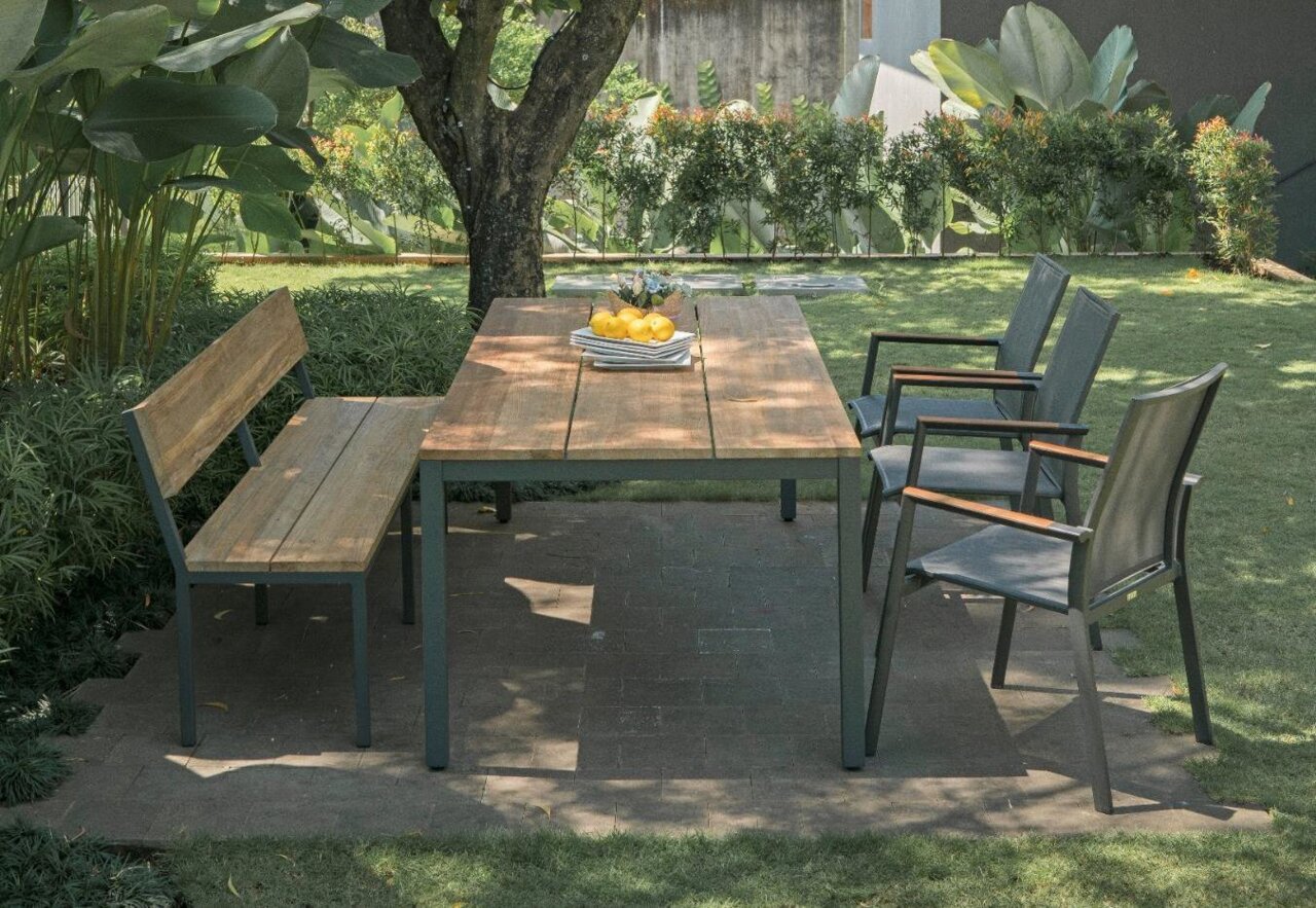 Gartenmöbel-Set mit einem Holztisch, einer Holzbank und drei Stapelsesseln aus Metall, seitliche Perspektive im Garten