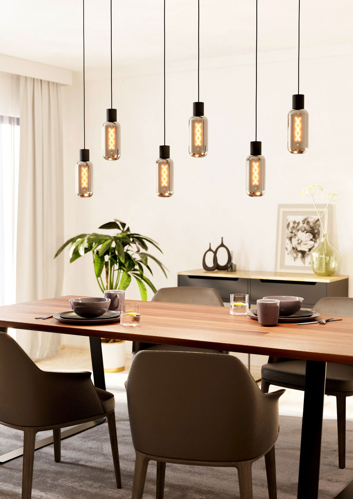 Moderne Pendelleuchte MAIONE mit sieben hängenden Glühbirnen über einem Esstisch, seitliche Perspektive.