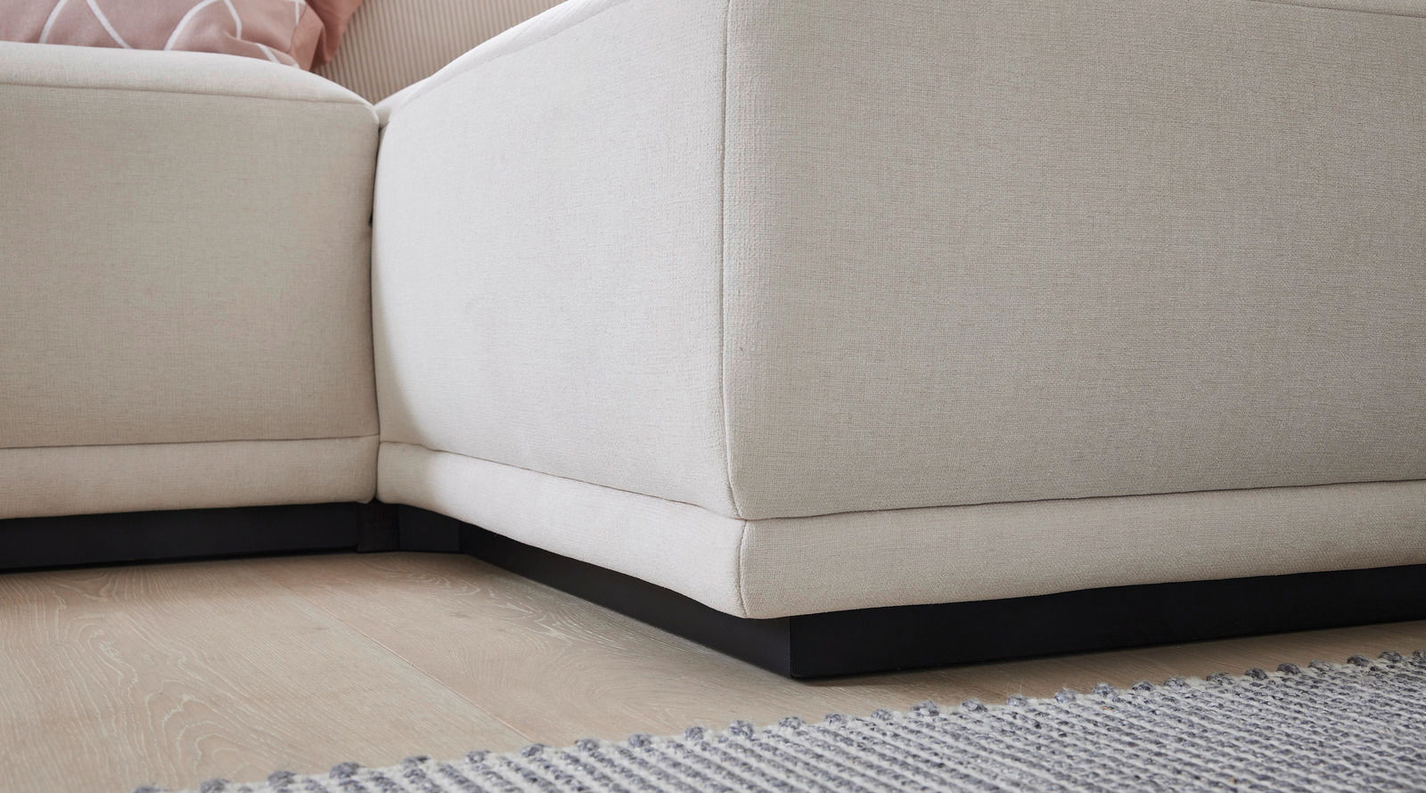 Nahaufnahme einer beigen Polsterecke des Musterring Ecksofas JUSTB! PM200, von unten fotografiert, mit einem Teil eines Teppichs im Vordergrund.
