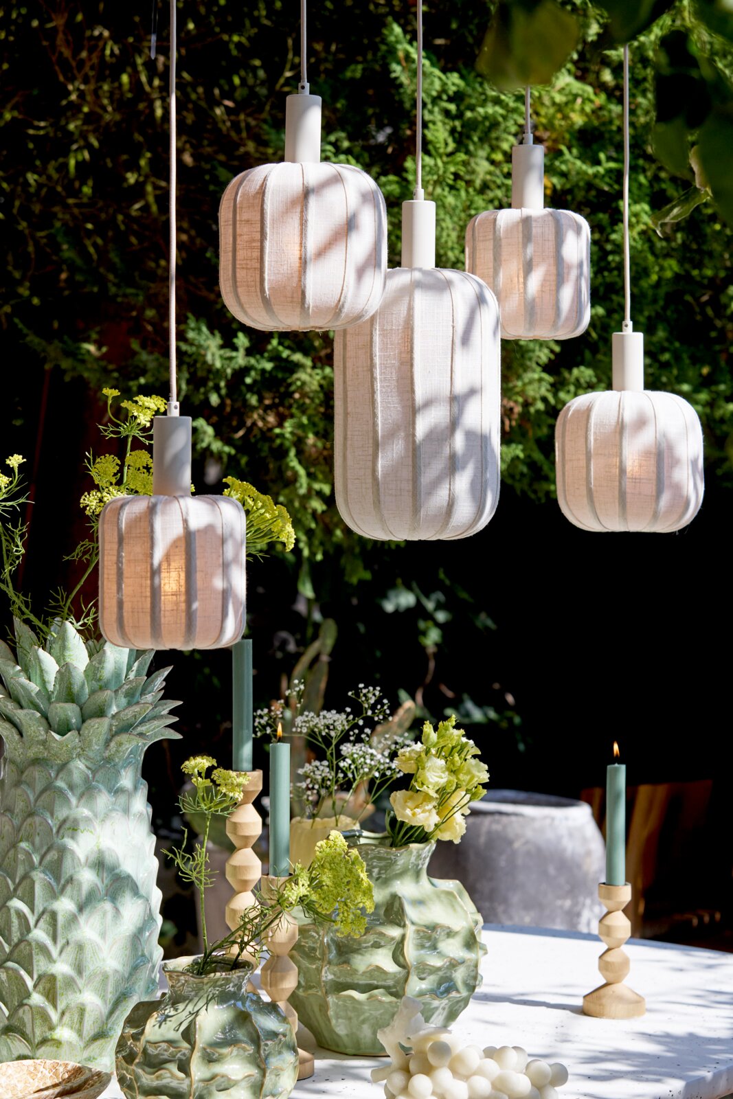 Een hanglamp in een tuin, omringd door groene planten en decoratieve vazen, gezien vanuit een laag standpunt.