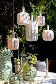 Een hanglamp in een tuin, omringd door groene planten en decoratieve vazen, gezien vanuit een laag standpunt.