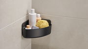 Schwarzer Eckduschkorb von tesa Lavaa, montiert in einer Badezimmer-Ecke, gefüllt mit Duschutensilien wie Flaschen und einem Schwamm, aus seitlicher Perspektive.
