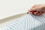 Nahaufnahme eines Tempur Topper Soft PRO PLUS SMARTCOOL mit geöffneter Reißverschlussabdeckung, die eine Hand zeigt, die den Reißverschluss zieht.