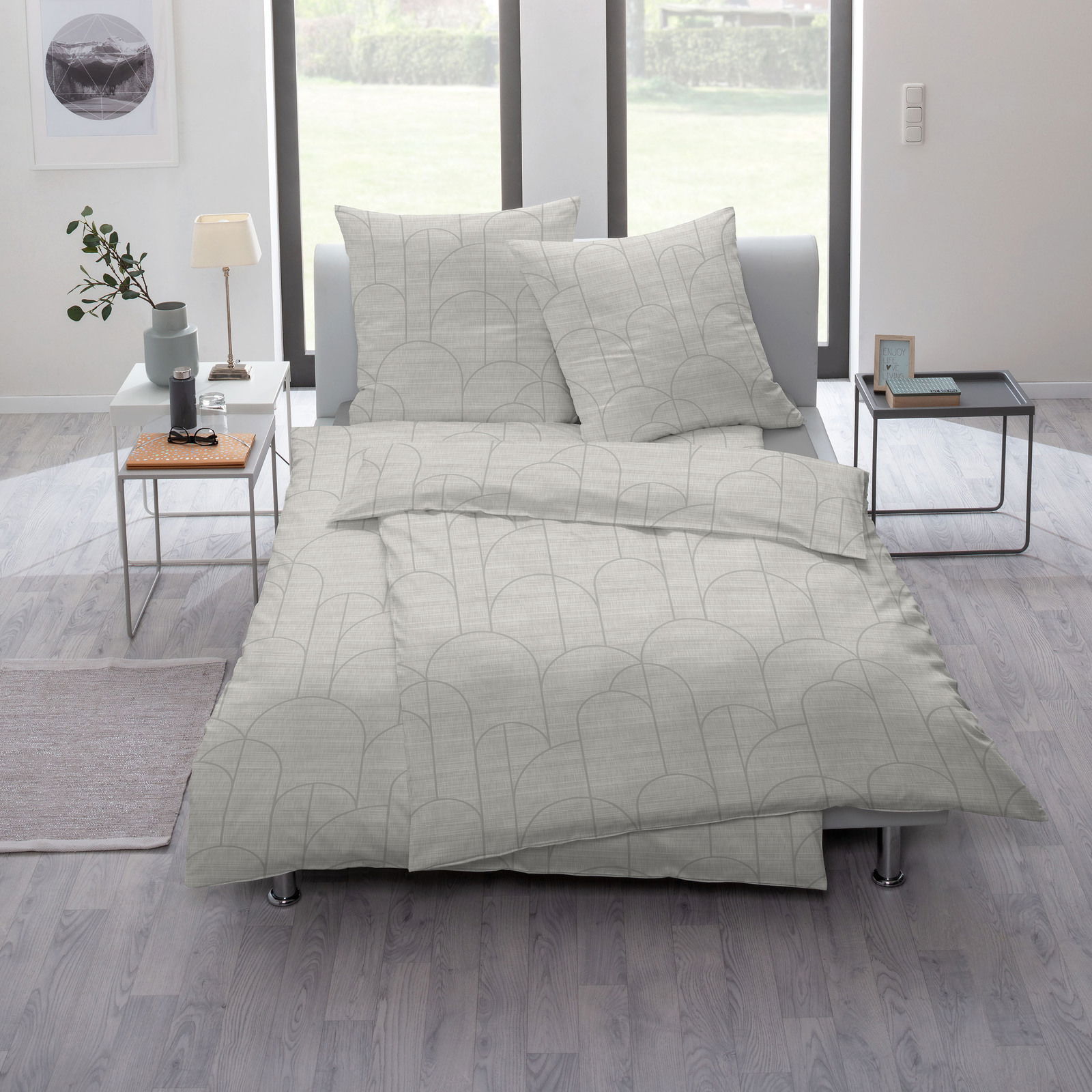 Bettwäsche-Set in modernem Design mit geometrischem Muster, auf einem Bett in einem hellen, minimalistischen Schlafzimmer mit großen Fenstern und stilvollen Beistelltischen präsentiert. Perspektive von vorne.