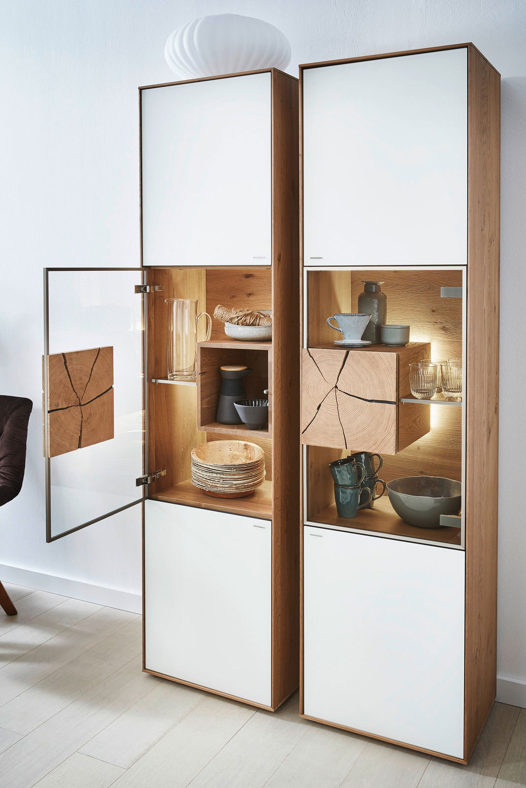 Vitrine Valnatura LAGO mit geöffneter Glastür, Holz- und Glaselementen, von links betrachtet.