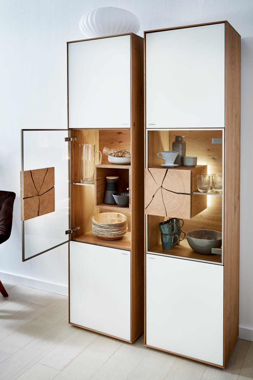 Vitrine Valnatura LAGO mit geöffneter Glastür, Holz- und Glaselementen, von links betrachtet.