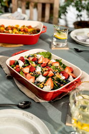 Rote Auflaufform mit frischem Salat aus Erdbeeren, Himbeeren, Blaubeeren, Walnüssen und Käse, auf einem gedeckten Tisch von oben fotografiert.