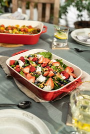 Een rode ovenschaal met een frisse salade van aardbeien, frambozen, bosbessen, walnoten en kaas, van bovenaf gefotografeerd op een gedekte tafel.