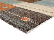 Nahaufnahme eines mehrfarbigen Frisé-Teppichs mit geometrischem Muster in Braun-, Beige- und Blautönen, perspektivisch von der Seite aufgenommen.