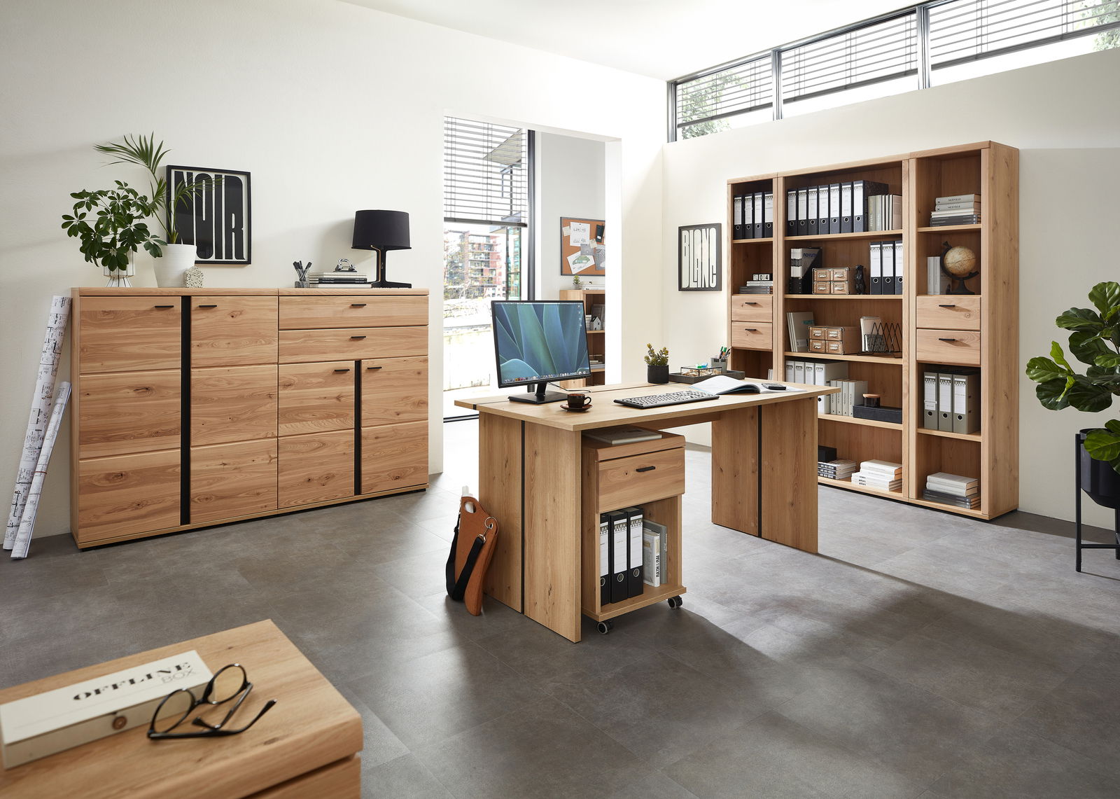 Moderne Büromöbel aus Holz in einem hellen Raum, bestehend aus einem Schreibtisch mit Rollcontainer, einem Aktenschrank und einem großen Regal. Perspektive von vorne.
