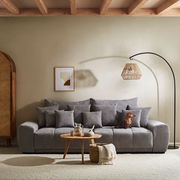 Großes graues Sofa TAVANI in einem gemütlichen Wohnzimmer, frontal fotografiert, mit mehreren Kissen und einem kleinen Hund darauf.